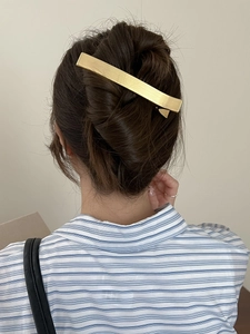 Vue détaillée d'une pince à cheveux minimaliste en métal doré brossé sur un chignon