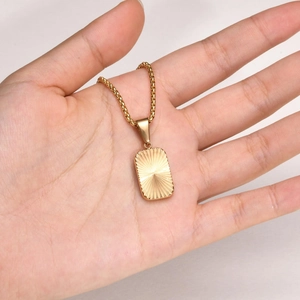 Macro view of golden rectangular pendant with sunburst texture held in hand for scale