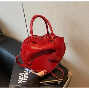 Détail d'un sac à main rouge en forme de cœur avec un grand nœud sur des livres