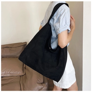 Detail of a large black suede tote bag featuring a wide shoulder strap in a minimalist style
