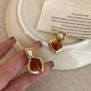 Detailed view of vintage gold earrings with amber resin stone and pearl stud