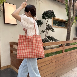 Outdoor lifestyle shot of a large red and white checkered canvas tote bag with wide straps