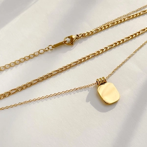 Detail of layered gold necklaces with geometric black agate pendant on white background
