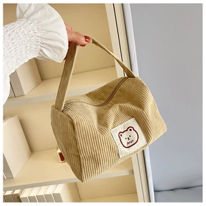 Close-up of khaki corduroy tote bag featuring a cute cartoon bear label with zipper detail