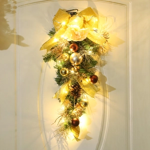 Festone natalizio dorato con luci LED, pigne e fiocchi appeso a una porta bianca