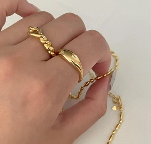 Detail of twisted and smooth gold knot rings with metallic gloss worn on finger
