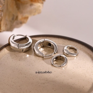 Macro view of four different sizes of polished silver hoop earrings on a ceramic dish