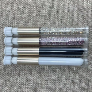 Close-up of four portable lip brushes with transparent tubes and gold metallic necks