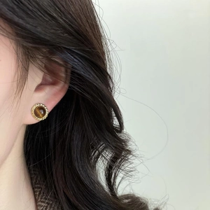 Golden woven frame tiger eye stone earring worn by a model with black hair in soft light