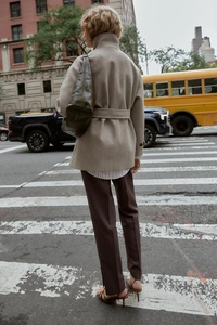Back view of a beige short wool coat with waist belt on a city street crossing