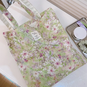 Dettaglio ravvicinato di una borsa tote in tela a fiori verde chiaro con oggetti quotidiani