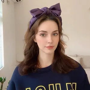 Elegant purple satin headband with a large bow design shown on a model for a slimming look