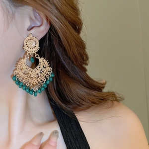 Detailed view of bohemian gold hollow drop earrings with green beads worn by a model