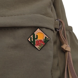 Macro detail of diamond-shaped desert sunset enamel pin on a green canvas backpack