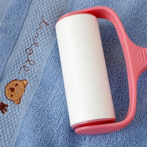Detail showing the pink lint roller cleaning a blue cotton towel with bear embroidery