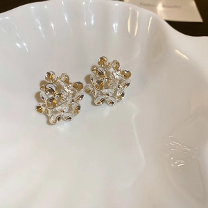 Macro shot of silver hollow flower stud earrings with intricate metallic petals on a shell plate