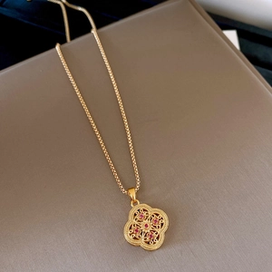 Close-up of vintage gold clover necklace with red gemstone and filigree details