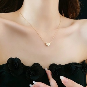 Detail of a textured golden heart pendant necklace worn on a model with black top