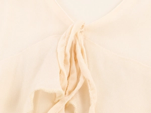 Dettaglio dello scollo a V di un abito in chiffon beige con volant e lacci decorativi