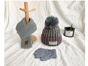Detailed view of kids knitted hat, scarf and gloves set in grey blue with pompom and tassels
