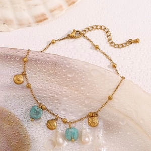 Detail of 18K gold shell and turquoise stone pendants on anklet over wet shell