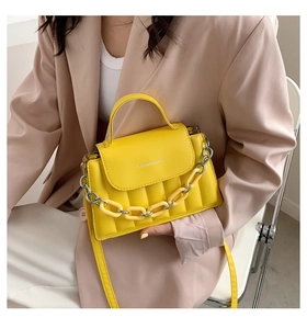 Close-up of yellow quilted crossbody bag with acrylic chain and top handle details