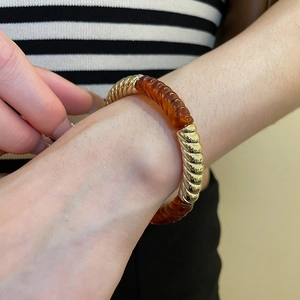 Detail of acrylic amber resin and gold-colored twisted metal sections on a modern bracelet