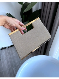 Detail of beige textured evening clutch featuring a stylish gold metal top handle