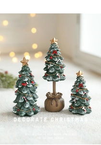 Three mini green Christmas trees with gold stars and candy canes on soft beige surface