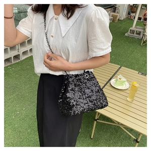 Outdoor view of a black sequin bucket bag with chain strap styled with summer attire