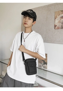 Close-up of a black nylon messenger bag worn by a model in a casual street style look