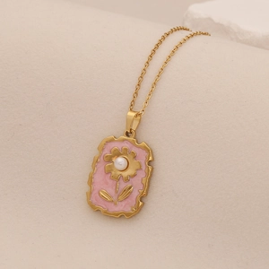 Gold sunflower pendant necklace with pink enamel and pearl on a textured stone background