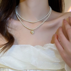 Close-up of double-layer pearl necklace featuring a golden heart pendant on model's neck