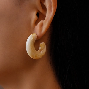Close-up of a beige marble acrylic C-shaped earring worn by a model in a luxury style