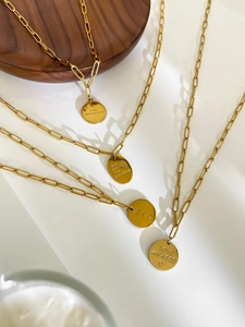 Detail of four golden paperclip necklaces with engraved coin pendants on white background