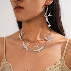 Detailansicht einer silbernen Schwalben-Halskette und Perlenohrringen an einem Model