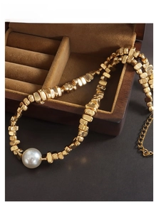 Detalle de un collar vintage dorado con eslabones irregulares y una gran perla redonda