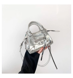 Detail of silver metallic handbag featuring studs, zippers, and a heart charm