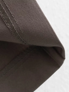 Detail showing high-quality double-needle stitching on brown minimalist trousers fabric