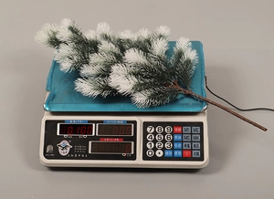Weight measurement of a snowy artificial pine branch decoration on a digital scale