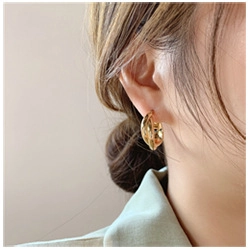 Close-up of a twisted 18k gold plated hoop earring on a model for a minimalist luxury look