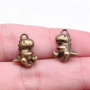Macro shot of two vintage bronze dinosaur pendants on a fingertip for size reference
