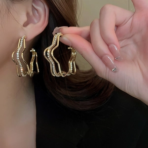 Elegant gold-tone layered wave earrings with sparkling rhinestones worn by a model