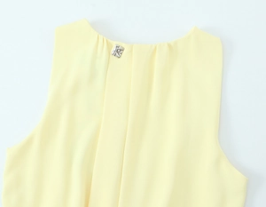 Close-up of light yellow midi dress neckline with silver square buckle and pleated detail