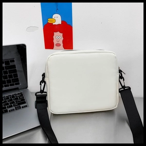 Detailed view of a white PU leather crossbody bag on a desk with adjustable black strap