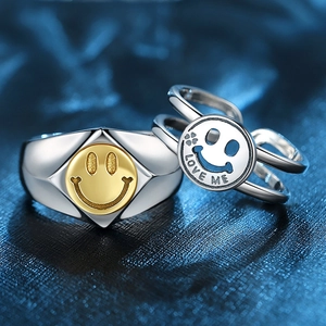 Macro detail of silver and gold smiley face rings with Love Me engraving on textured background