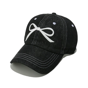 Detail of white bow embroidery and contrast stitching on a black denim baseball cap