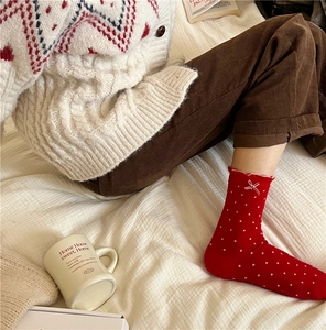 Detail of red crew socks with white polka dots, lace trim and bow, worn in cozy home setting