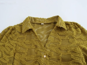 Detail of mustard yellow textured fabric shirt with V-neck and pearl button closure
