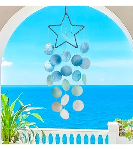 Star-shaped shell wind chime with blue gradient discs hanging against a sea view balcony